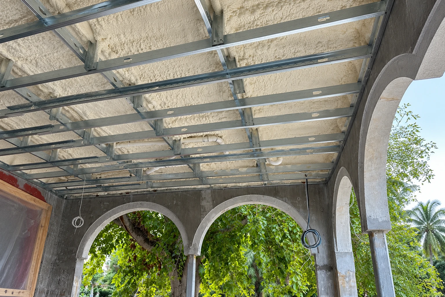 White spray foam coats the underside of a ceiling framed with metal channels above open arches.