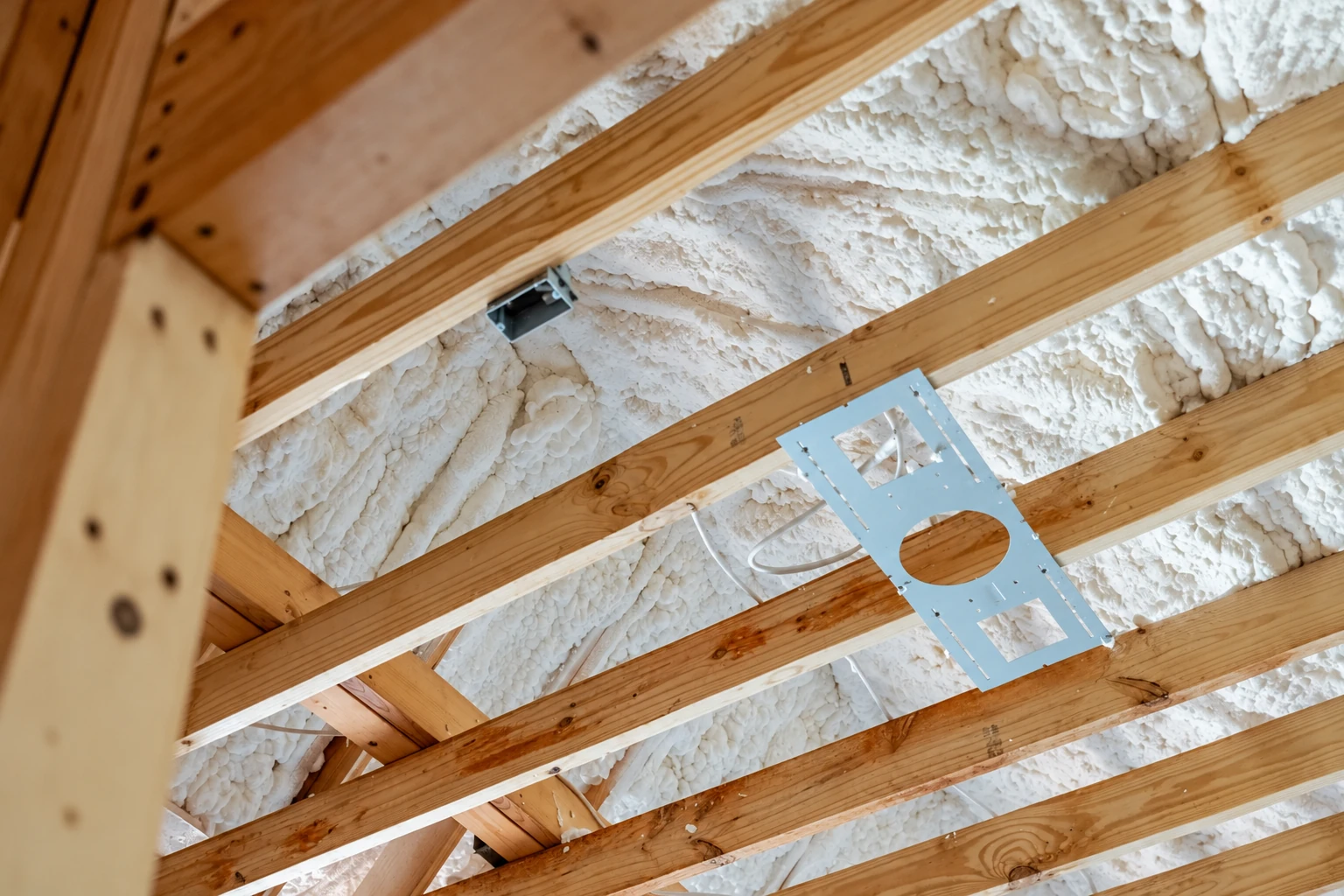 Close view of white spray foam insulation filling the spaces between exposed wooden roof rafters.