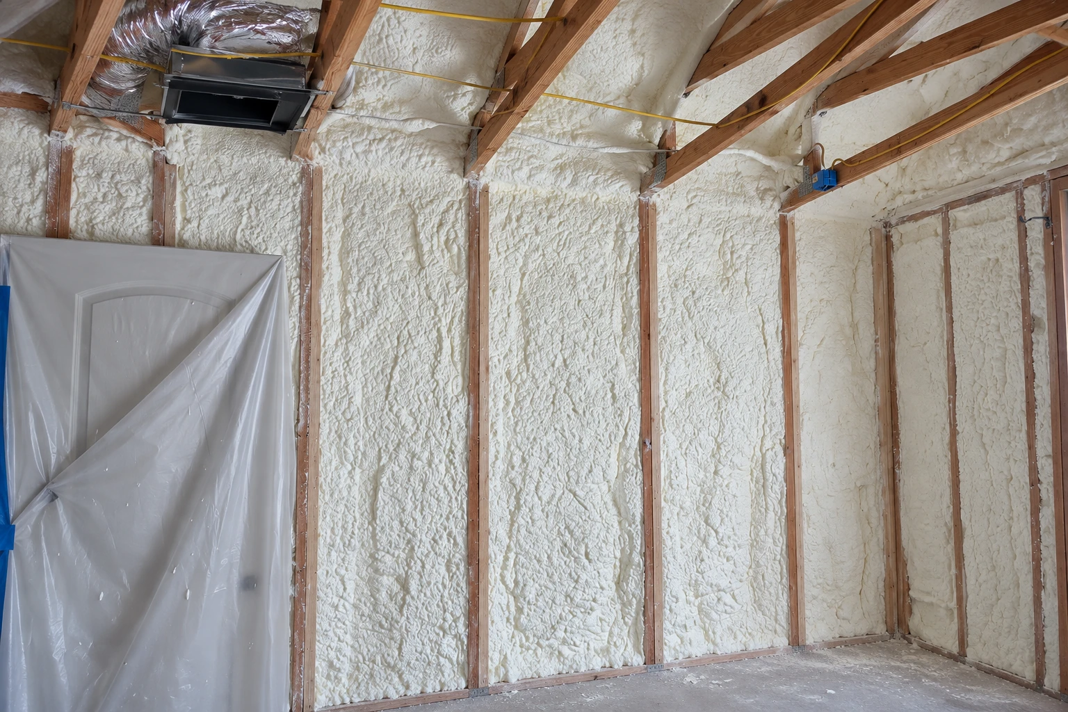 Open-cell spray foam coats the walls and ceiling between exposed wooden studs in an unfinished room.